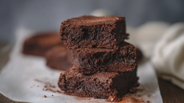 Brownie de chocolate recién horneado con helado y nueces, servido en un plato blanco.