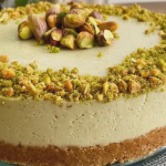 Rebanada de cheesecake fría de pistachos decorada con pistachos y crema de pistacho sobre un plato.
