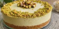 Rebanada de cheesecake fría de pistachos decorada con pistachos y crema de pistacho sobre un plato.