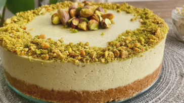 Rebanada de cheesecake fría de pistachos decorada con pistachos y crema de pistacho sobre un plato.