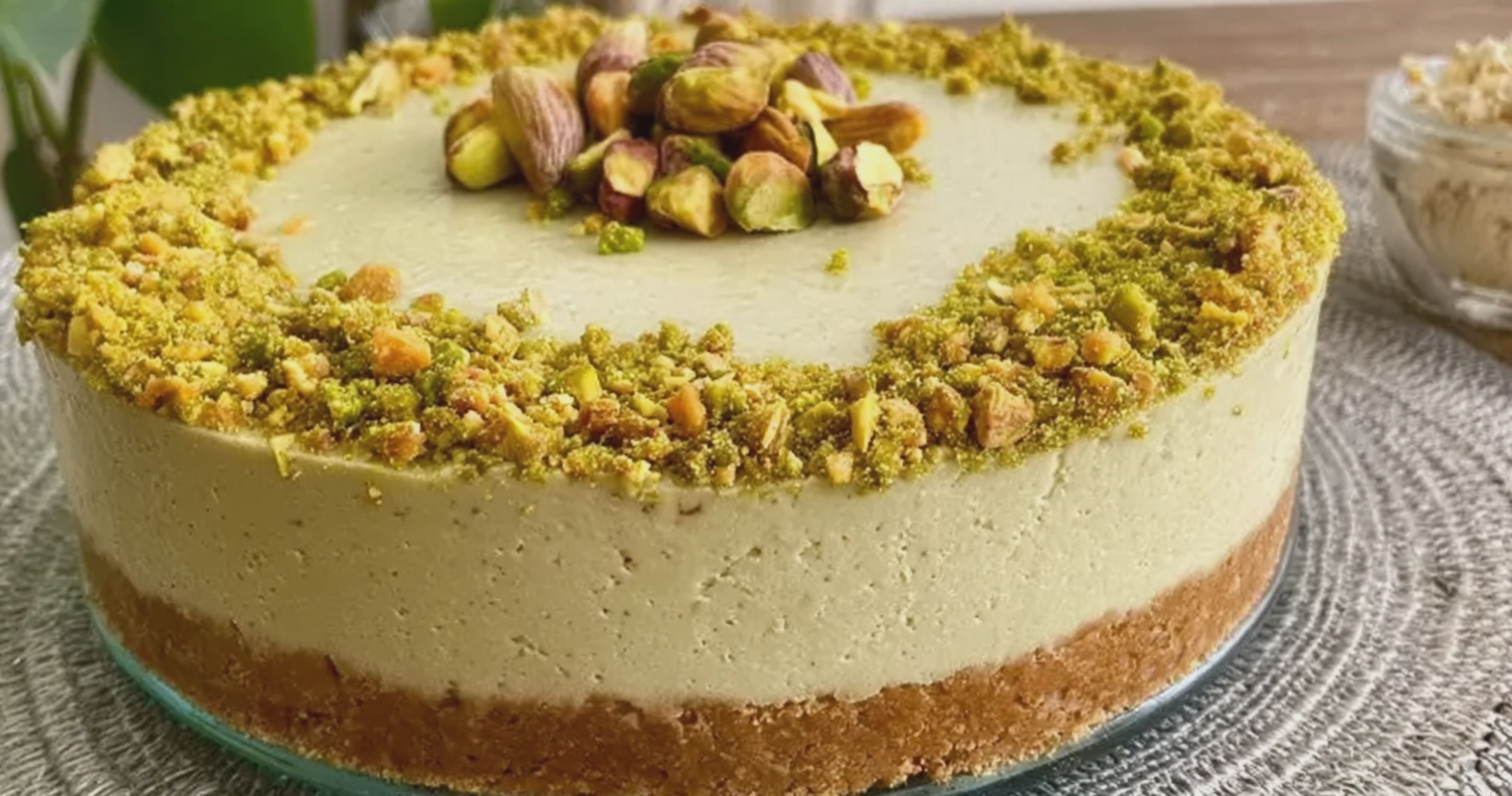 Rebanada de cheesecake fría de pistachos decorada con pistachos y crema de pistacho sobre un plato.
