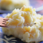 Puré de papas con crema de ajo servido en un tazón, decorado con perejil fresco en una mesa rústica.