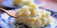 Puré de papas con crema de ajo servido en un tazón, decorado con perejil fresco en una mesa rústica.